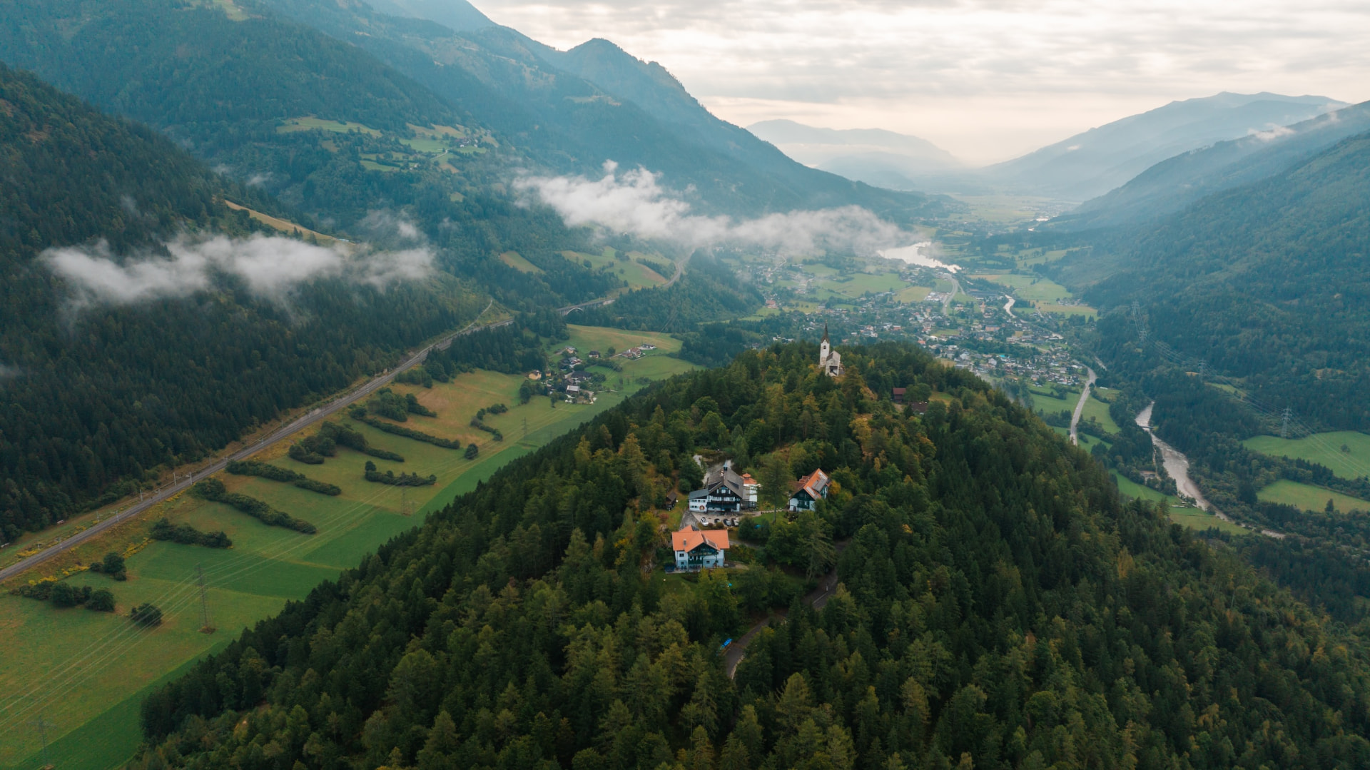 Der Danielsberg mit Herkuleshof und Kirche aus der Luft, im Hintergrund das Mölltal mit Wolken