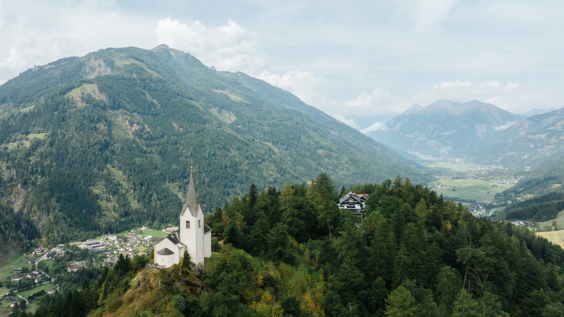 Kirche St. Georg und Herkuleshof auf dem bewaldeten Danielsberg, dahinter das Tal