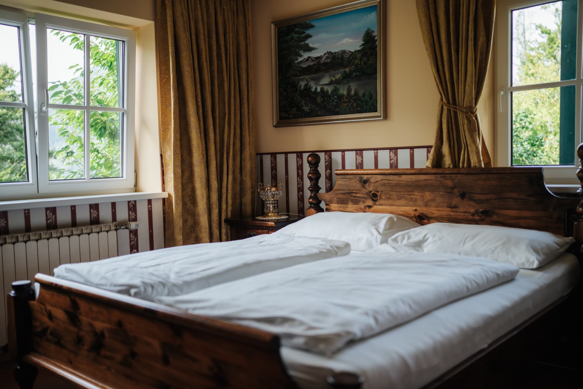 Helles Zimmer am Herkuleshof mit Holzbett, Bergbild und zwei Fenstern