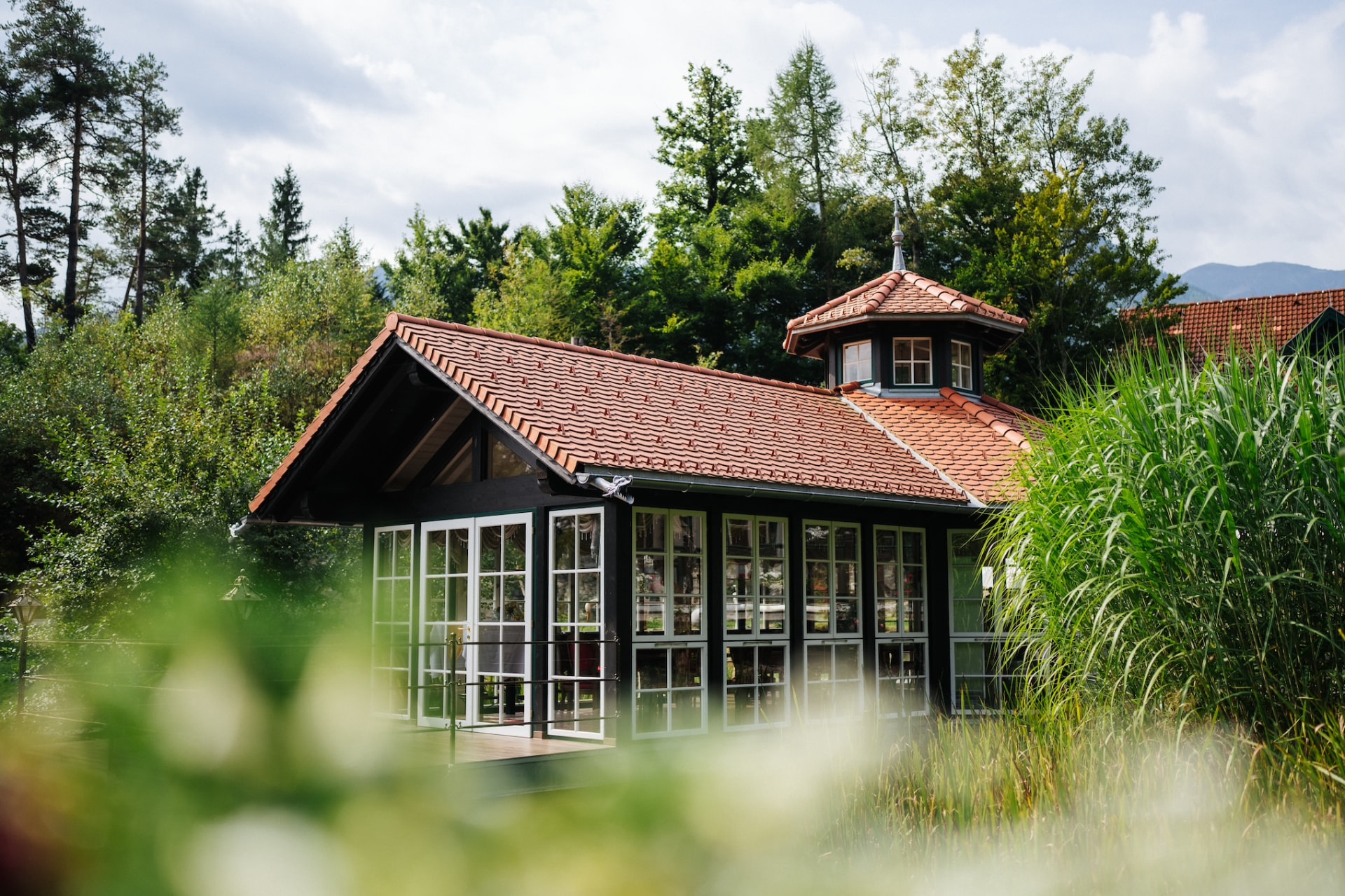 Der Glaspavillon am Herkuleshof inmitten von Bäumen und Gräsern